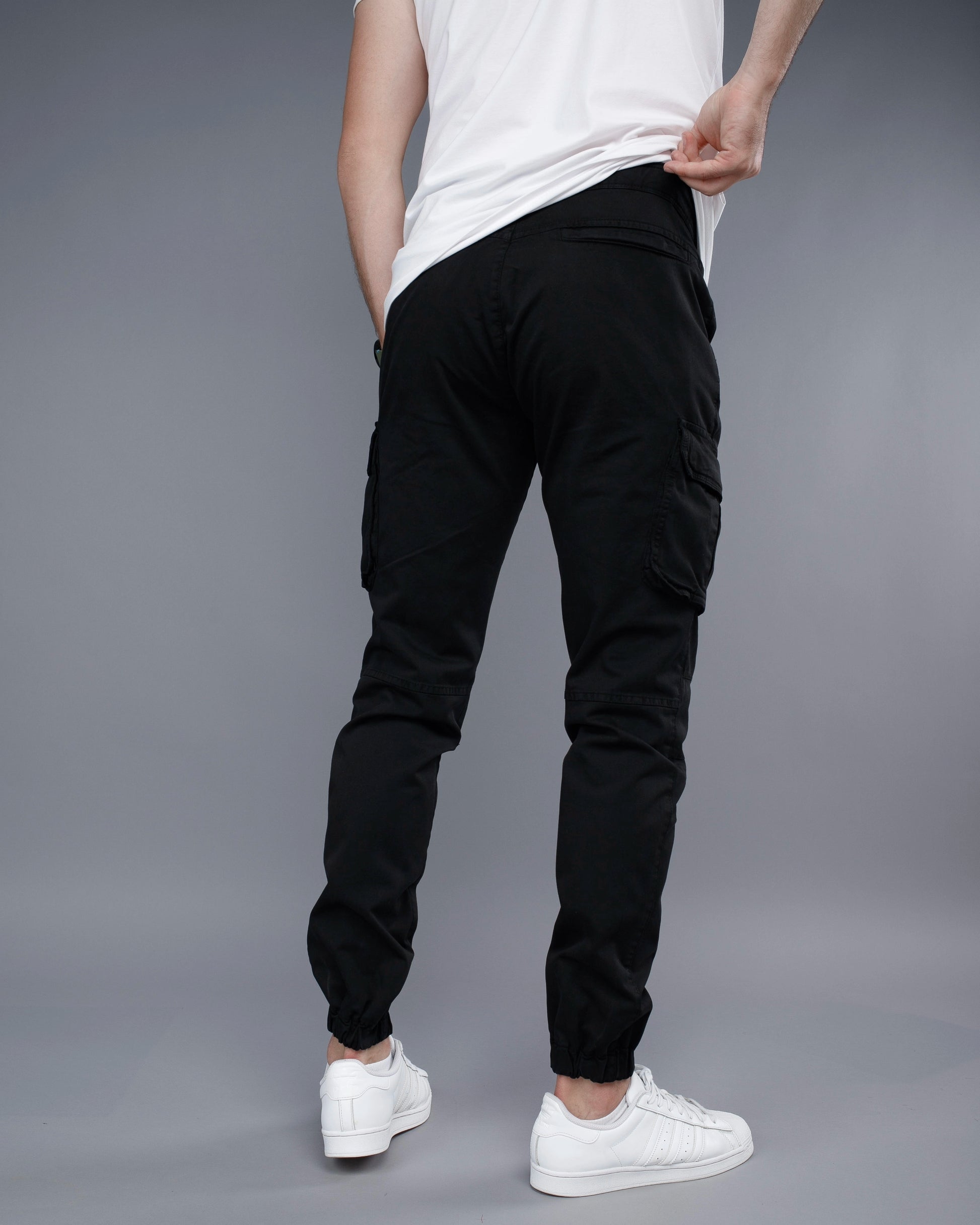 Person wearing black jogger pants and white sneakers on a gray background