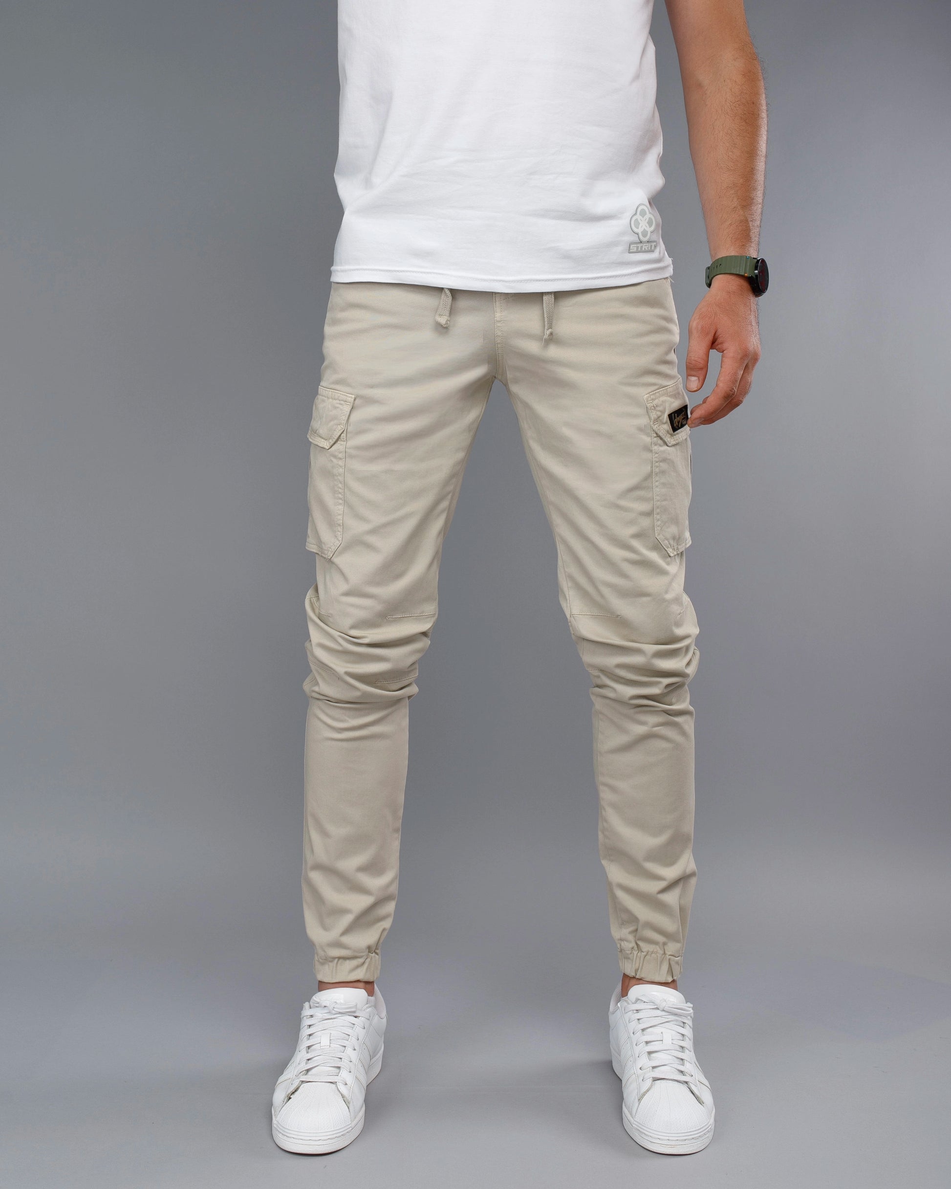 Person wearing beige cargo pants and white sneakers on a gray background