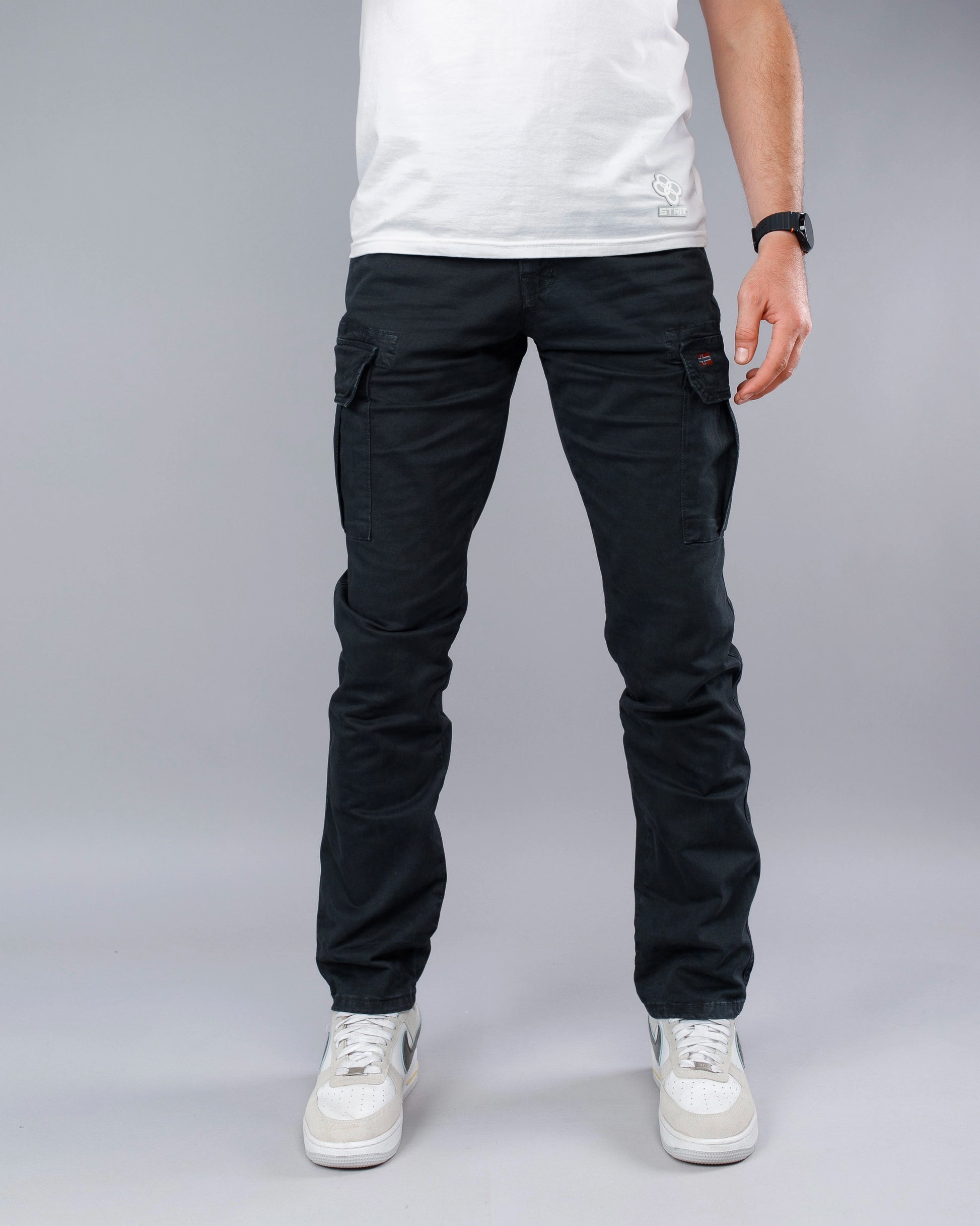 Person wearing black cargo pants and white sneakers on a gray background