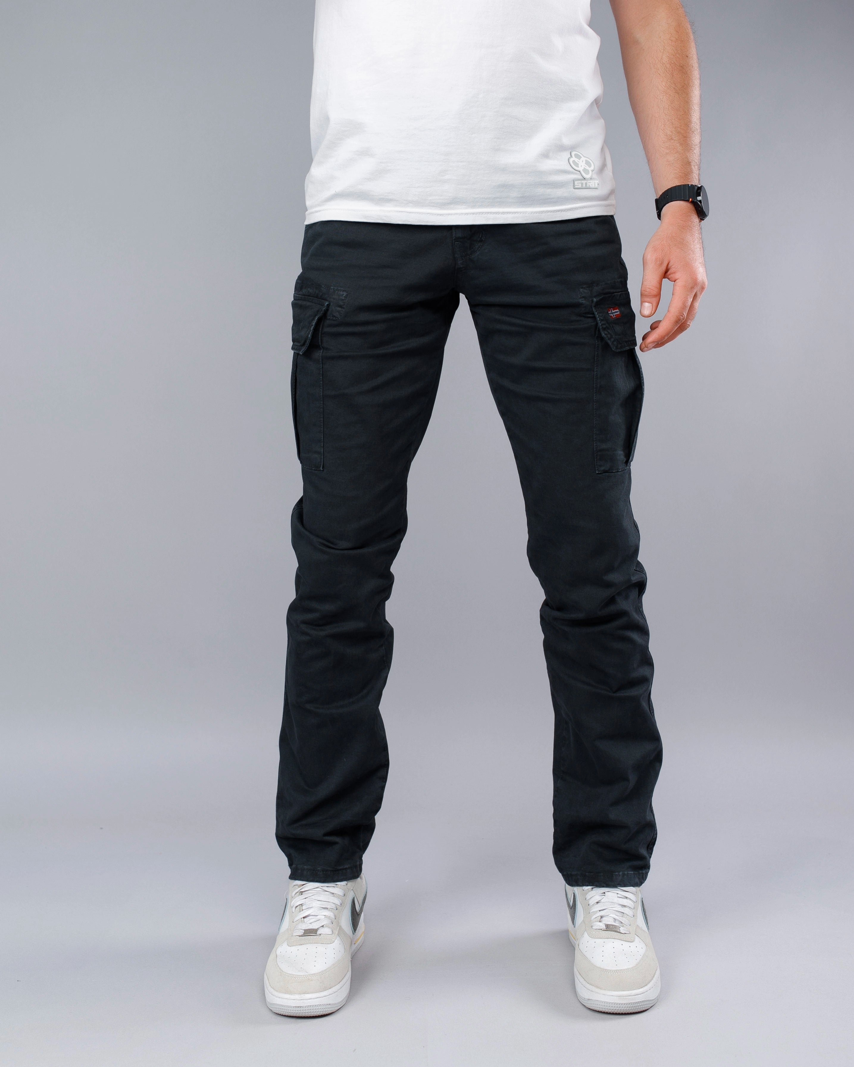 Person wearing black cargo pants and white sneakers on a gray background