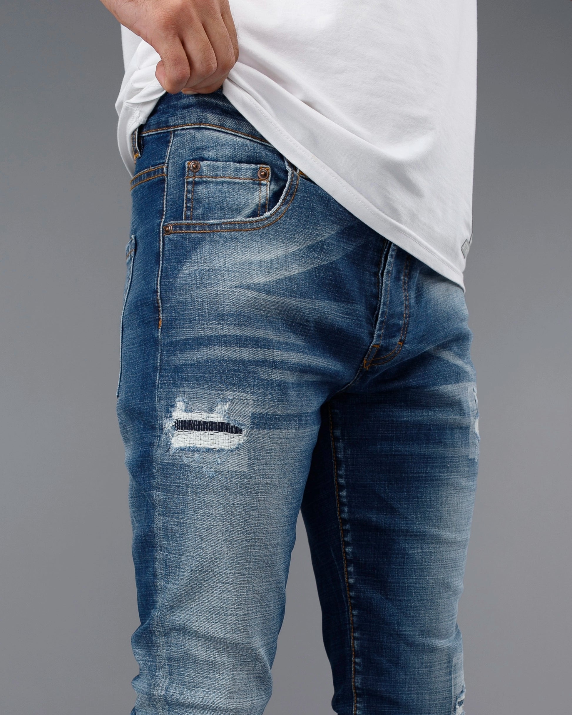 Blue distressed jeans worn by a person on a gray background
