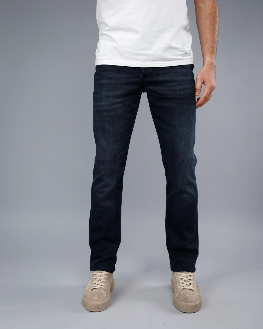 Person wearing dark jeans and a white shirt on a gray background