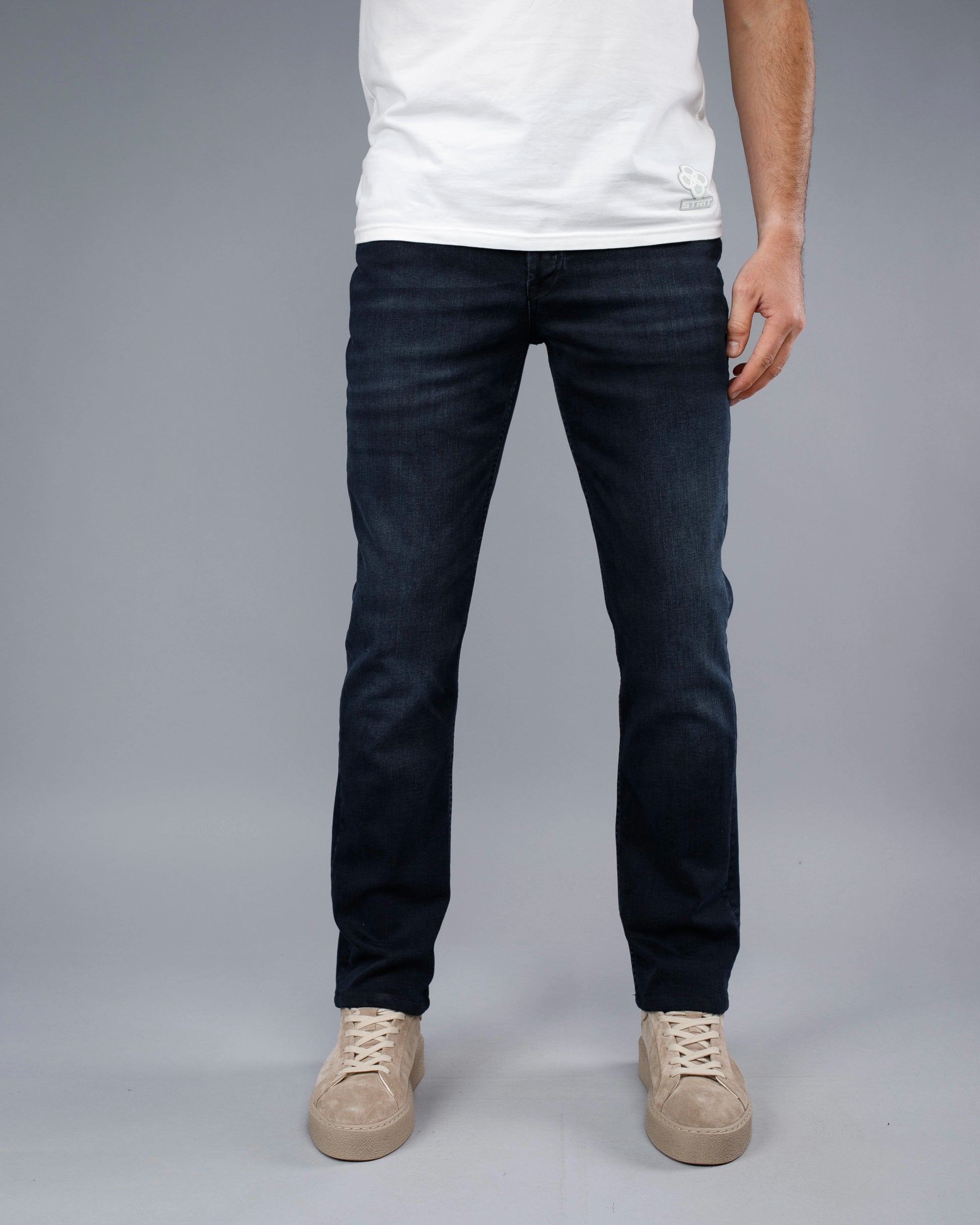 Person wearing dark jeans and a white shirt on a gray background