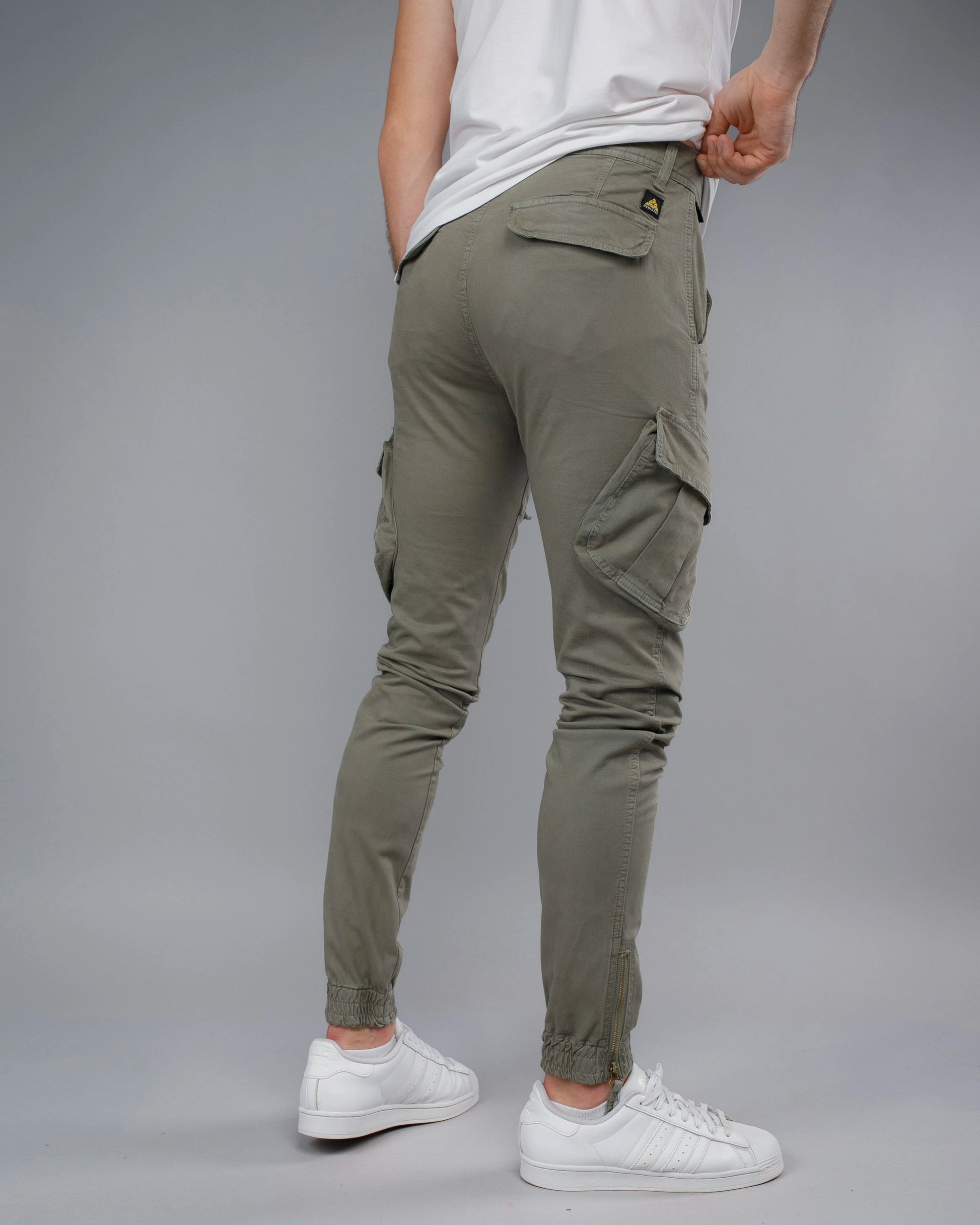 Person wearing olive green cargo pants and white sneakers on a gray background