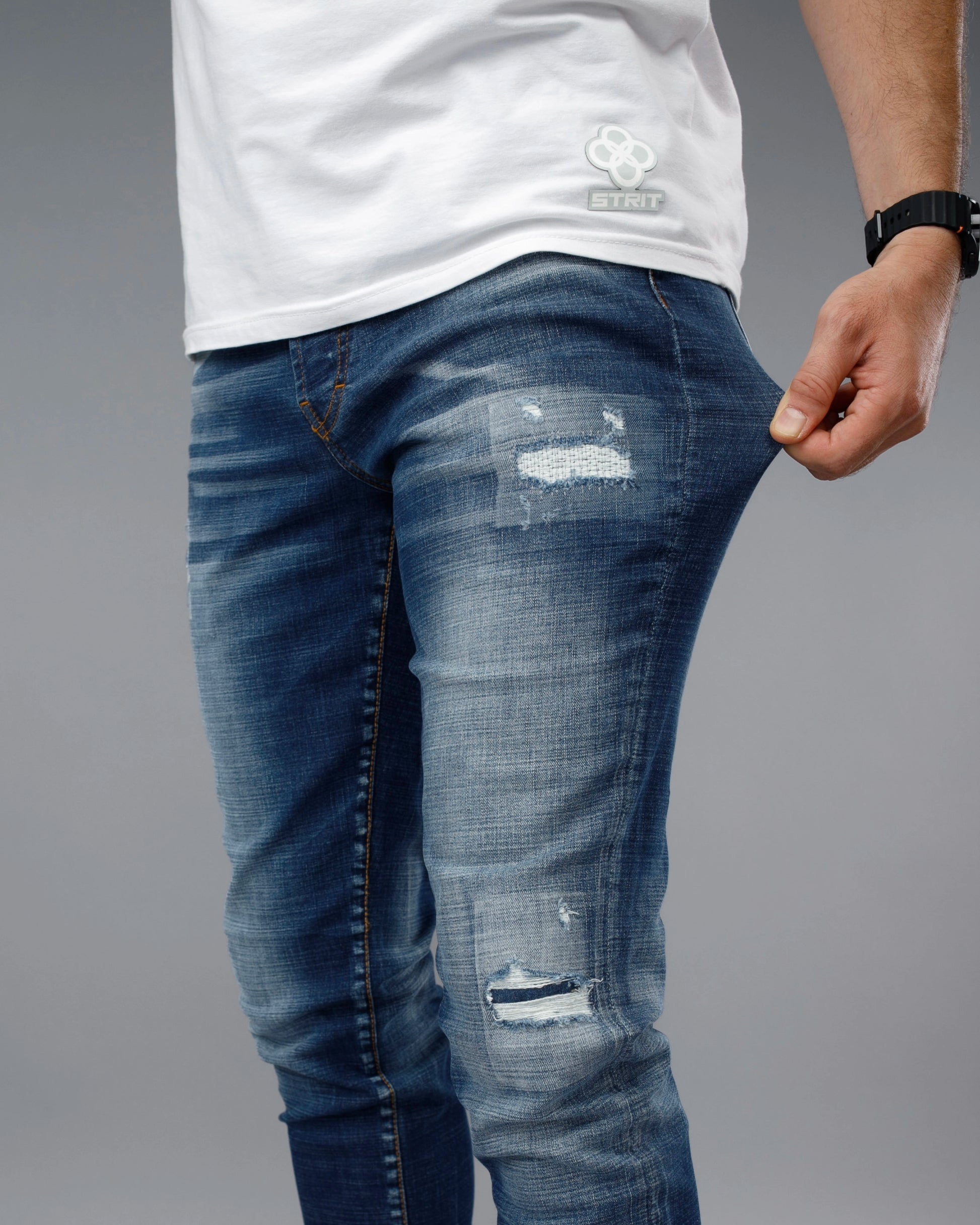 Person wearing distressed blue jeans and a white t-shirt on a gray background