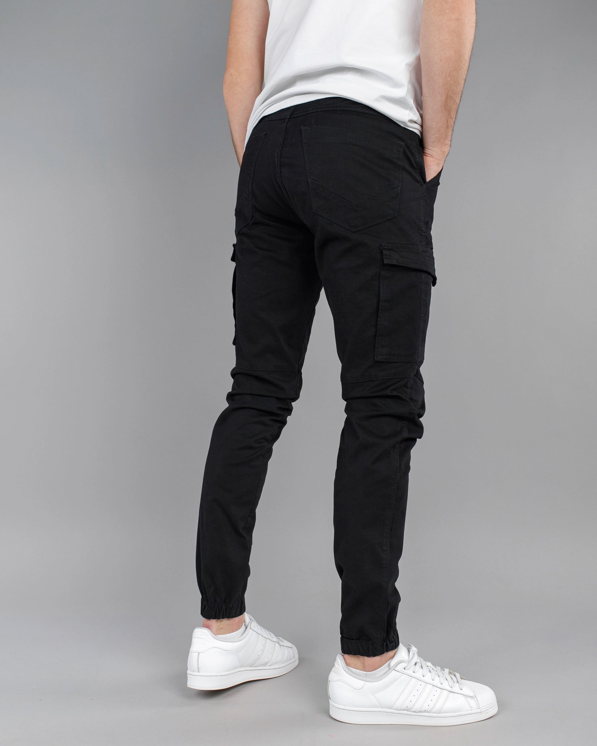 Person wearing black cargo pants and white sneakers on a gray background