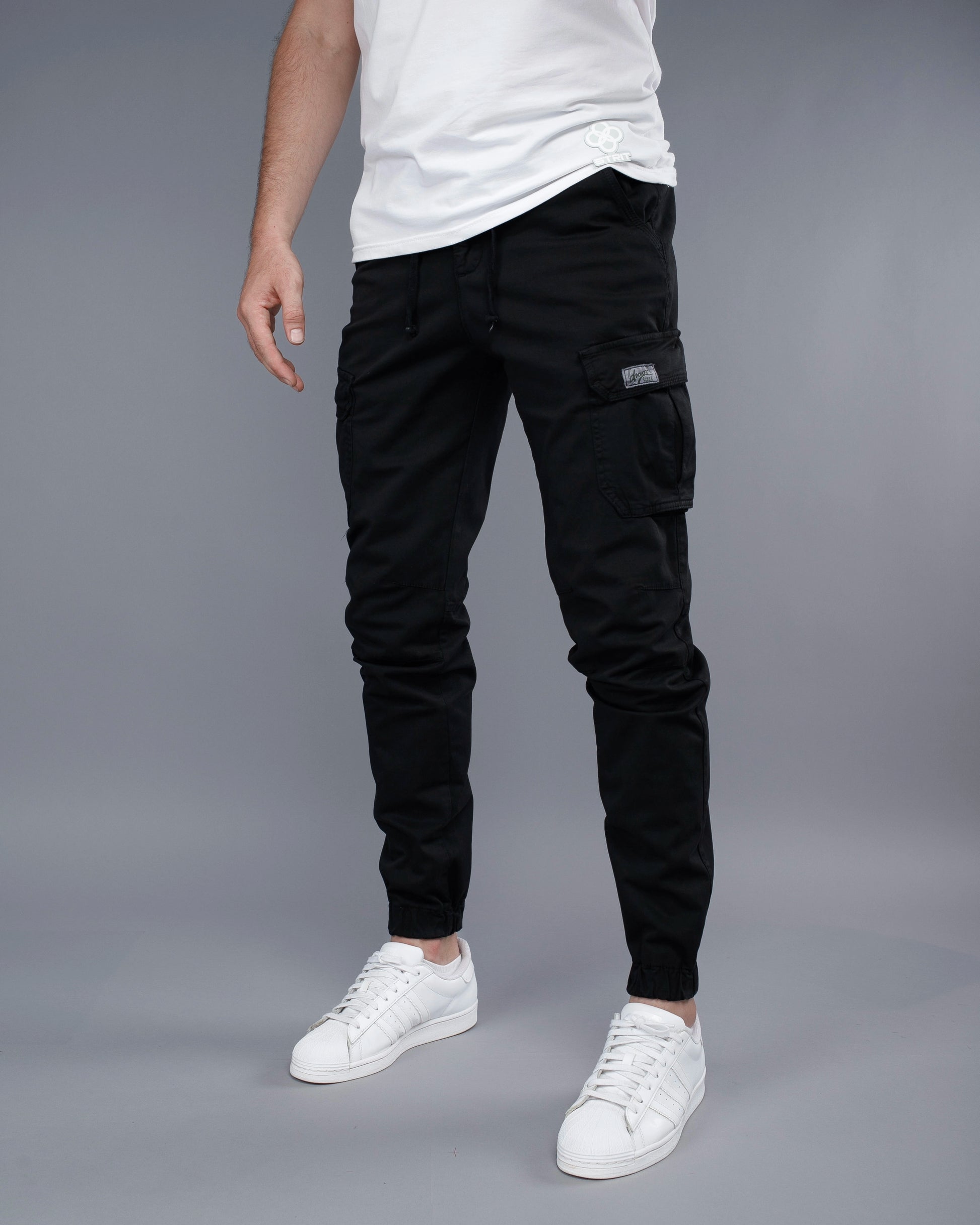 Person wearing black cargo pants and white sneakers on a gray background
