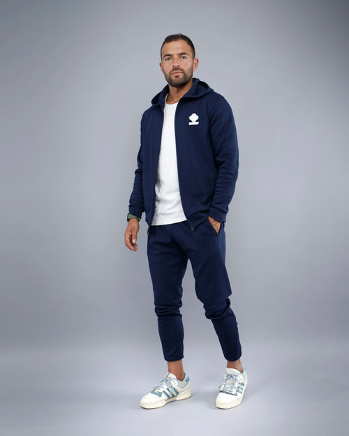 Man wearing a navy tracksuit with a logo on a gray background