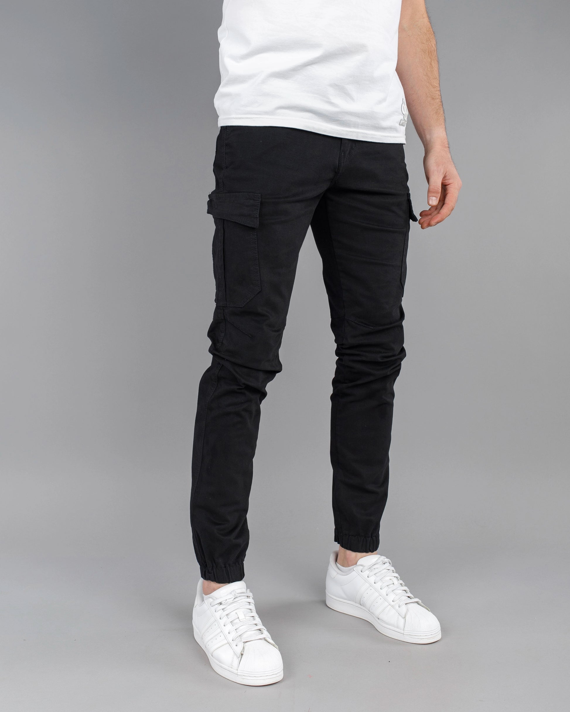 Person wearing black cargo pants and white sneakers on a gray background
