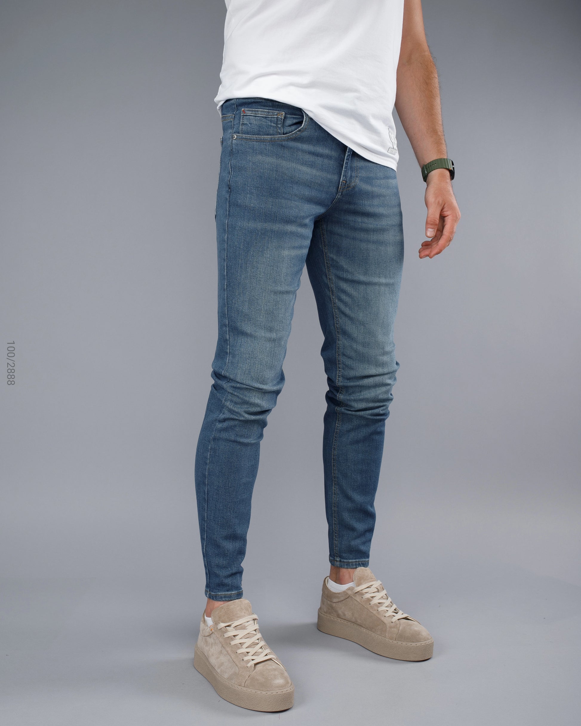 Person wearing blue jeans and beige sneakers on a gray background