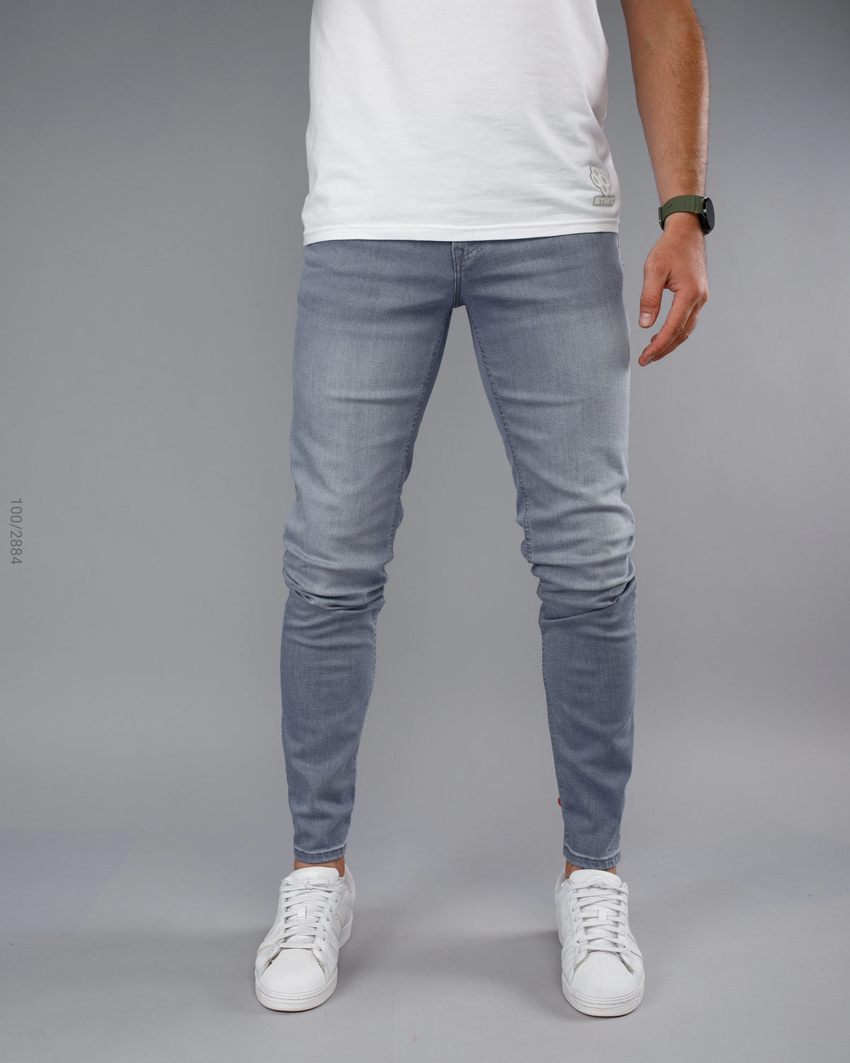 Person wearing light blue jeans and white sneakers on a gray background