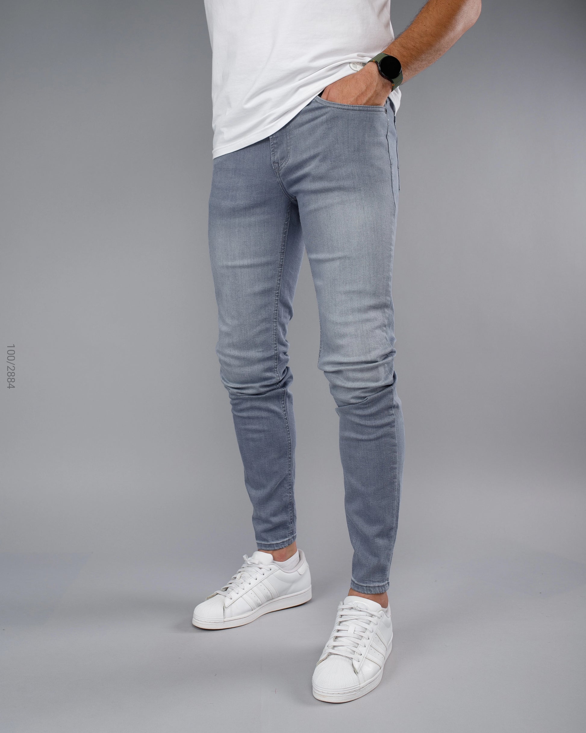 Person wearing light blue jeans and white sneakers on a gray background
