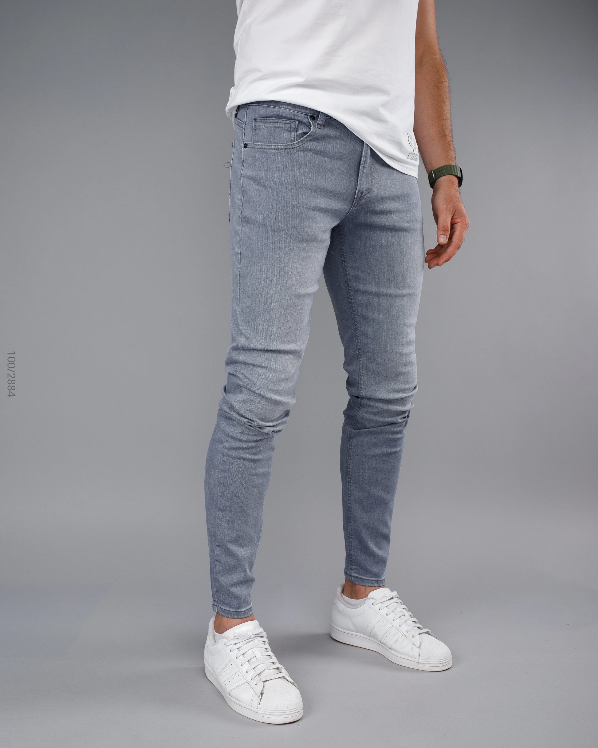Person wearing light blue jeans and white sneakers on a gray background