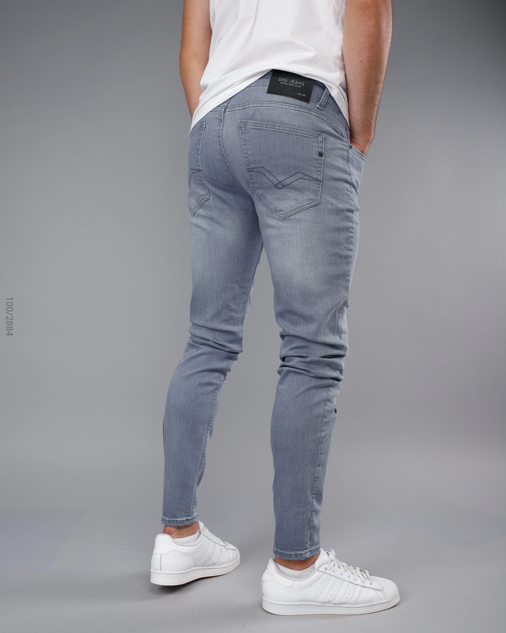 Person wearing light blue jeans and white sneakers on a gray background