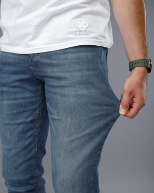 Person wearing blue jeans and a white shirt with a logo on a gray background
